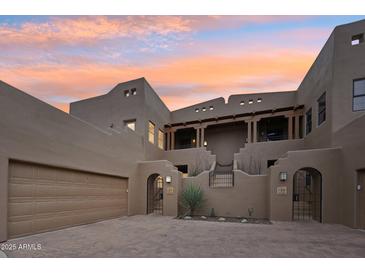 Elegant multi-story home with arched gated entry and covered balcony, set against a vibrant sunset sky at 36601 N Mule Train Rd # C38, Carefree, AZ 85377