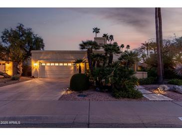 Inviting single-Gathering home featuring a two-car garage, tropical landscaping, and warm exterior lighting at twilight at 8737 E San Vicente Dr, Scottsdale, AZ 85258