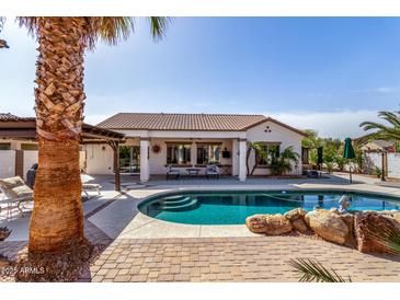 Stunning backyard pool, complemented by a covered patio, lush palm trees, and comfortable lounge chairs at 16438 W Mescal St, Surprise, AZ 85388