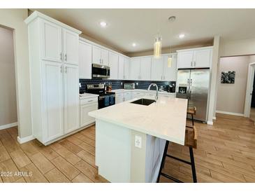 Modern kitchen features white cabinets, stainless steel appliances, a large island with barstool seating, and wood flooring at 155 N Lakeview Blvd # 207, Chandler, AZ 85225