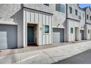 View of the home's stucco exterior, light-gray garage door, and the quaint blue door and decorative brick pathway at 2228 W Harmont Dr, Phoenix, AZ 85021