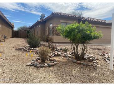 Tan single-story home featuring a tile roof, a two-car garage, and a gravel yard with shrubbery at 43857 W Bedford Dr, Maricopa, AZ 85138