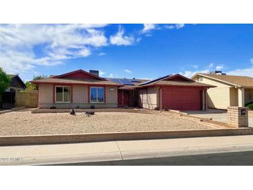 Charming single-story brick home with a red trim, gravel yard, and solar panels under a clear blue sky at 13834 N 39Th Ln, Phoenix, AZ 85053