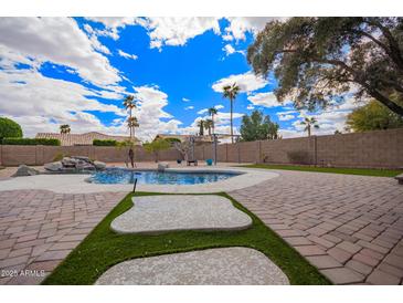 The backyard features a luxurious pool, lush greenery, and a charming pergola for outdoor enjoyment at 14609 W Marcus Dr, Surprise, AZ 85374