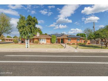 Charming brick home featuring a well-manicured lawn, solar panels, and mature trees on a sunny day at 1610 E Mclellan Rd, Mesa, AZ 85203