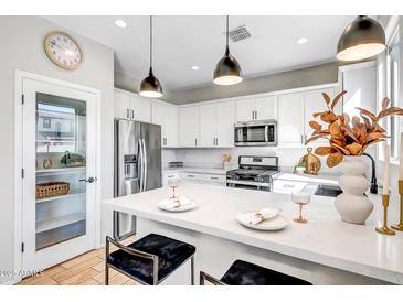 Bright, white kitchen with stainless steel appliances and a large island featuring stylish pendant lighting at 10823 W Polk St, Avondale, AZ 85323