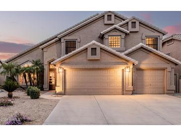 Inviting two-story home with a three-car garage, desert landscaping, and a warm, welcoming glow at dusk at 12955 E Mercer Ln, Scottsdale, AZ 85259