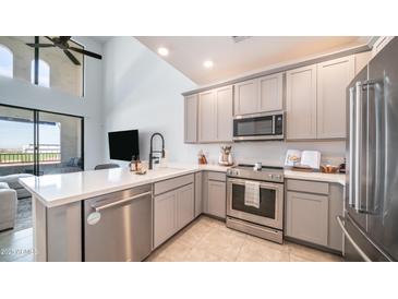 A modern kitchen featuring stainless steel appliances, gray cabinetry, and a breakfast bar overlooking the living area at 2511 W Queen Creek Rd # 479, Chandler, AZ 85248