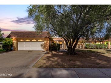 Charming single-story brick home with a two-car garage and mature landscaping at dusk at 9730 W Gulf Hills Dr, Sun City, AZ 85351