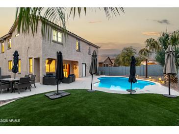 Relaxing backyard featuring a sparkling pool, artificial grass, and comfortable outdoor seating at twilight at 3603 S Weaver E Cir, Gilbert, AZ 85297