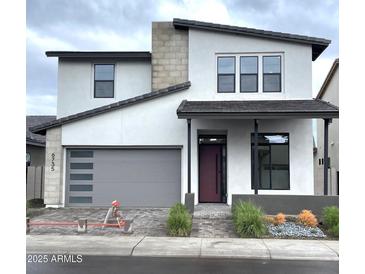 Modern two-story home with a gray garage door, brick driveway, xeriscaped front yard, and a covered porch at 6735 N 9Th Dr, Phoenix, AZ 85013