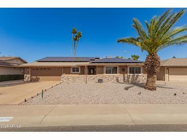 Charming single-story home featuring modern stone accents and solar panels against a bright blue sky at 10718 W Saratoga Cir, Sun City, AZ 85351