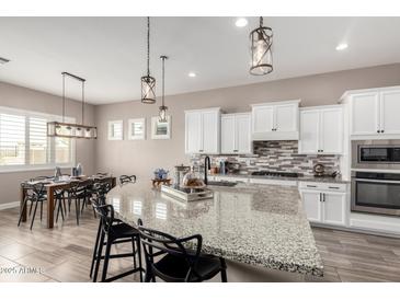Open kitchen layout features island seating, white cabinetry, stainless appliances, and modern lighting at 9302 W White Feather Ln, Peoria, AZ 85383