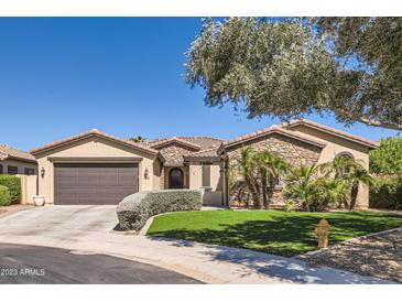 Charming single-story home featuring a stone facade, manicured landscaping, and a spacious driveway at 14870 W Aldea Cir, Litchfield Park, AZ 85340