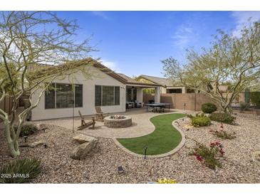 A cozy backyard featuring a stone fire pit, seating, artificial turf, desert landscaping, and mature trees at 2544 W Pumpkin Ridge Dr, Anthem, AZ 85086