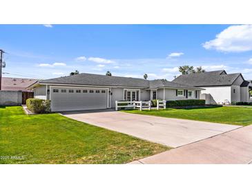 Charming single-story home with a gray exterior, lush green lawn, and a driveway leading to an attached two-car garage at 4239 E Mitchell Dr, Phoenix, AZ 85018