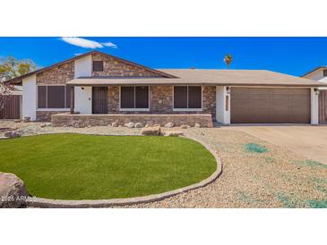 Charming stone-accented home with a manicured lawn and a two-car garage, nestled under a clear blue sky at 17408 N 14Th Ave, Phoenix, AZ 85023