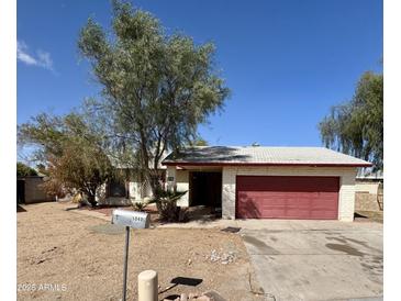 A single-story home boasts a red two-car garage door, desert landscaping, and mature trees under a bright blue sky at 5040 N 69Th Dr, Glendale, AZ 85303