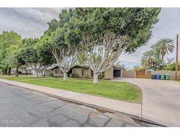 Charming single-story home featuring mature trees, lush lawn, and a long driveway leading to a garage at 1035 W 2Nd St, Mesa, AZ 85201