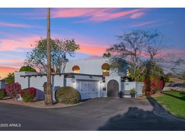 Charming white home featuring a gated entrance, two-car garage, and colorful desert landscaping at dusk at 8001 N 3Rd Pl, Phoenix, AZ 85020