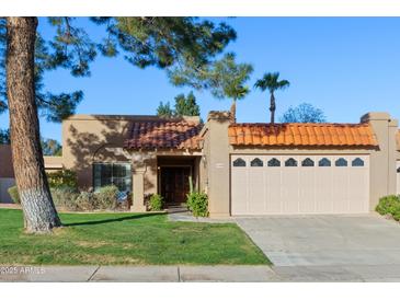 Charming home featuring a red tile roof, two-car garage, and a well-maintained front lawn with mature landscaping at 9088 E Winchcomb Dr, Scottsdale, AZ 85260