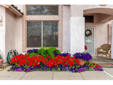 Charming home entrance featuring vibrant flower beds and a cozy wicker chair at 8568 W Purdue Ave, Peoria, AZ 85345