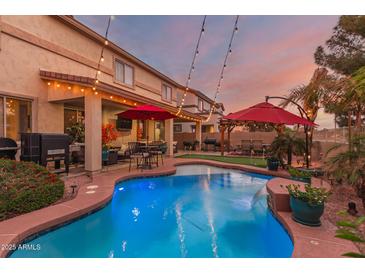 Beautiful backyard oasis with a sparkling blue pool, lush landscaping, and outdoor seating area with a red umbrella at 17541 W Statler Dr, Surprise, AZ 85388