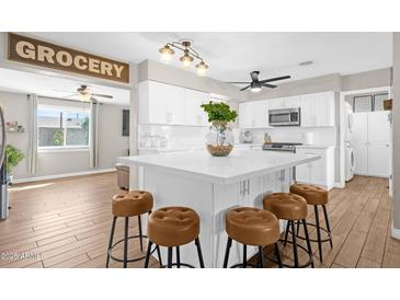 Bright kitchen featuring white cabinets, center island with seating, and modern appliances, complemented by wood-look flooring at 1715 W Carol Ave, Mesa, AZ 85202