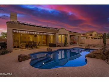Inviting backyard pool with rock features, covered patio, and seating under a sunset sky at 9604 S 183Rd Dr, Goodyear, AZ 85338