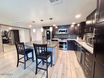 Contemporary kitchen boasts wooden floors, dark cabinets, island with pendant lighting and stainless steel appliances at 7920 E Camelback Rd # 203, Scottsdale, AZ 85251