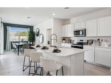 Modern white kitchen with an island, seating, stainless steel appliances, and stylish light fixtures at 23984 W Cocopah St, Buckeye, AZ 85326