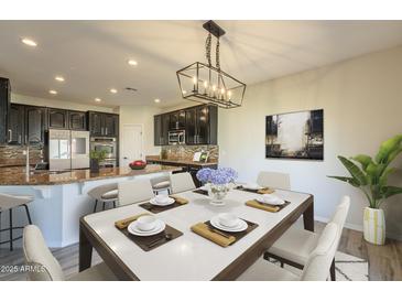 An open-concept kitchen flows into a dining area with seating for six beneath a modern chandelier at 16462 W Rowel Rd, Surprise, AZ 85387