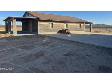 Side exterior view showcasing the concrete driveway that leads to the block constructed house with tile roof at 9600 S 393Rd Ave, Tonopah, AZ 85354