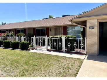 Charming single-story home featuring a well-maintained lawn, mature landscaping, and secure decorative metal fencing at 10327 W Prairie Hills Cir, Sun City, AZ 85351