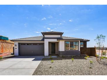 Inviting single-story home featuring a gray garage door, stone accents, and a well-maintained gravel yard at 5875 N 193Rd Dr, Litchfield Park, AZ 85340