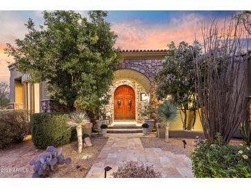 Elegant front entrance with stone archway, a carved wooden door, desert landscaping, and a stone paver walkway at 10040 E Happy Valley Rd # 269, Scottsdale, AZ 85255