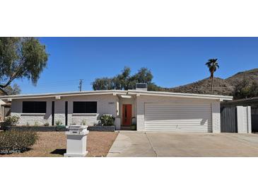 Charming single story white brick home with a tidy landscaped yard and a bright orange front door at 12807 N 21St Dr, Phoenix, AZ 85029