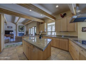Open kitchen featuring an island with granite countertops, wooden beams, stainless appliances, and light wood cabinetry at 8619 E Silver Saddle Dr, Carefree, AZ 85377