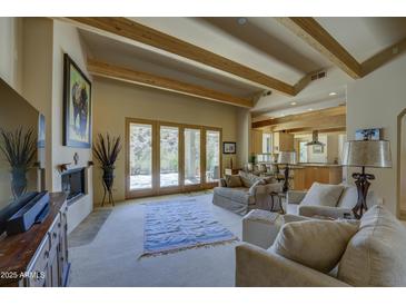 Spacious living room with wooden beams, a fireplace, comfortable seating, and patio access, perfect for relaxation and entertaining at 8619 E Silver Saddle Dr, Carefree, AZ 85377