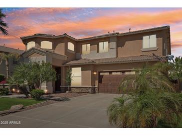 Exterior view of home featuring lush landscaping, an attached garage, and a colorful sunset backdrop at 18504 W Maui Ln, Surprise, AZ 85388