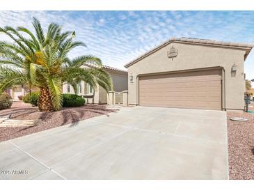 Beige single-story home featuring a two-car garage, concrete driveway, and mature palm tree in landscaped front yard at 21026 N Circle Cliffs Dr, Surprise, AZ 85387