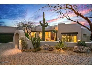 Stylish desert home featuring an arched entryway, mature cacti, and inviting outdoor lighting at 39912 N 98Th Way, Scottsdale, AZ 85262