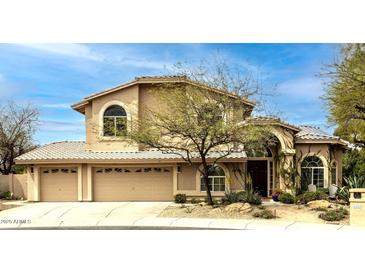 A tan stucco home has a three car garage and arched front entry, along with desert landscaping at 6828 E Evans Dr, Scottsdale, AZ 85254