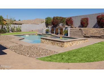 Inviting pool with a waterfall feature and integrated spa, surrounded by well-maintained landscaping at 7024 W Tether Trl, Peoria, AZ 85383