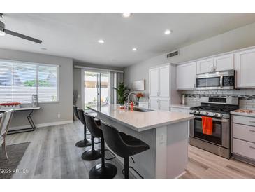 Bright kitchen featuring a large island with seating, stainless steel appliances, and sliding glass doors leading to the patio at 17988 W Deneen Way, Surprise, AZ 85374