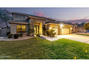 Charming home exterior with well-manicured lawn, warm lighting, and a three car garage at 69 E Benrich Dr, Gilbert, AZ 85295