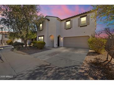Two-story home featuring a desert-style landscape and a two car garage is awash in pink light from the setting sun at 17043 N Avelino Dr, Maricopa, AZ 85138