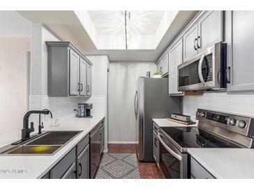 Galley kitchen features gray cabinets, stainless appliances, white countertops, tile backsplash and a stylish skylight at 3830 E Lakewood E Pkwy # 2042, Phoenix, AZ 85048