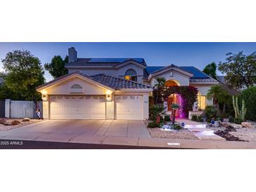 Charming home featuring a three-car garage, solar panels, and inviting entrance with lush landscaping at twilight at 1614 E Kathleen Rd, Phoenix, AZ 85022