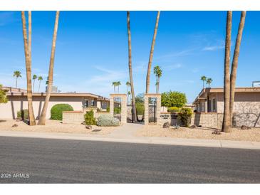 A street view of the Cactus Court community entrance with brick walls and iron gates, surrounded by palm trees and lush landscaping at 16827 N 103Rd Ave, Sun City, AZ 85351